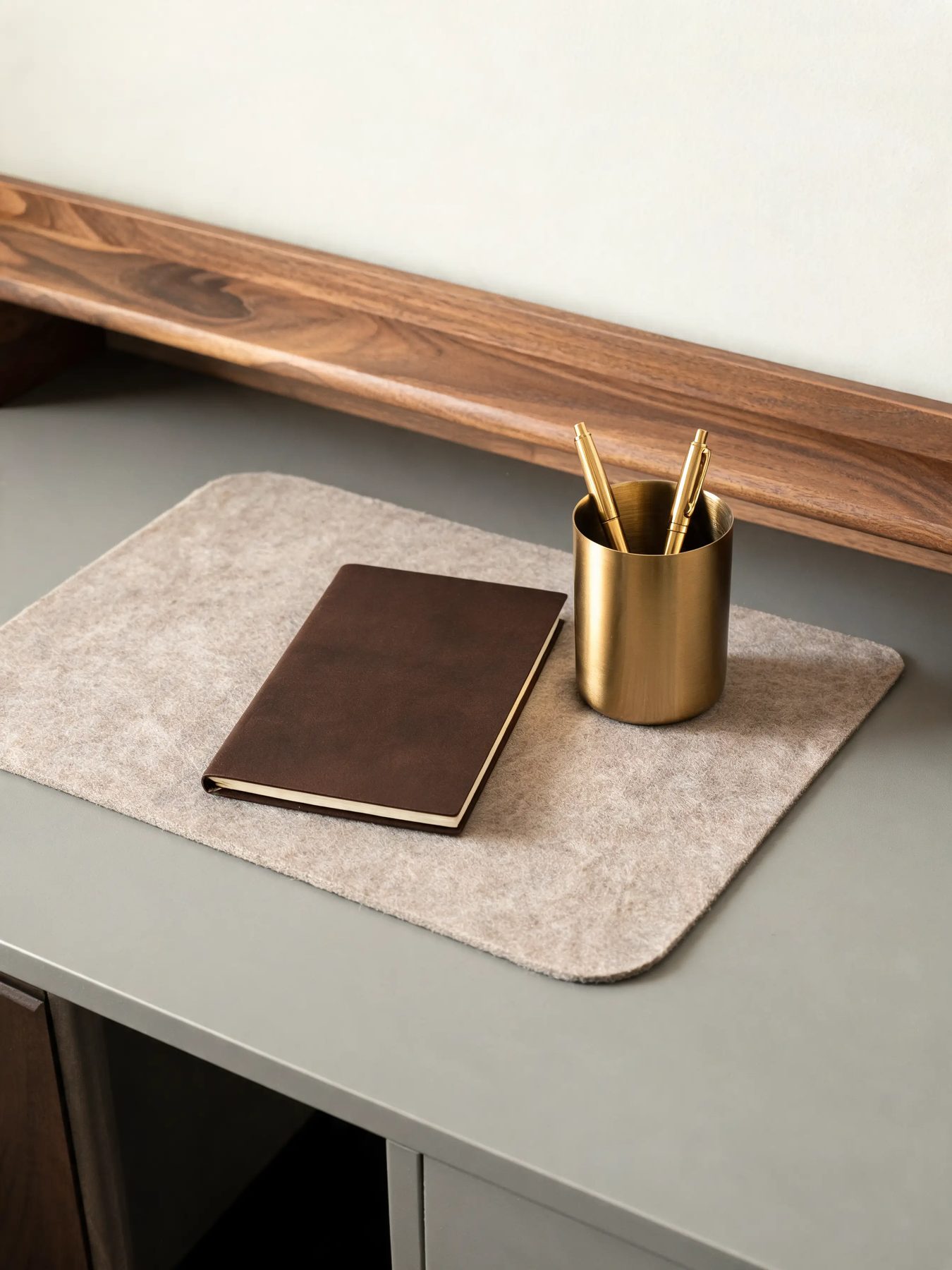 Walnut desk shelf with a felt mat and a brass pen cup on a matte grey desk